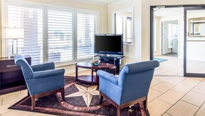 Un salon moderne avec deux fauteuils bleus, une table basse de couleur sombre, un téléviseur à écran plat et un tapis orné de motifs en forme d’étoiles.