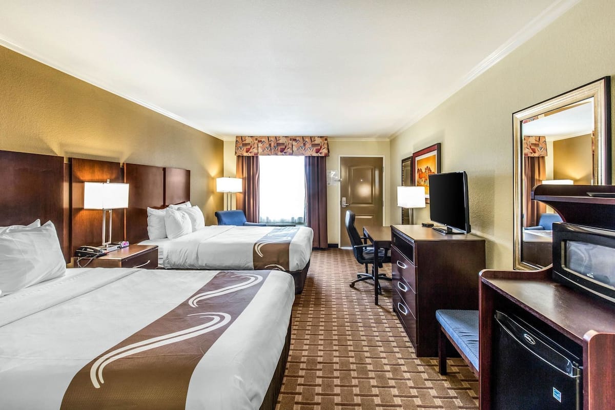 A hotel room with two beds, a desk with a television, a chair, and a desk lamp.