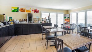 Un restaurant doté d’un comptoir de cuisine, de tables, de chaises et offrant une vue sur l’extérieur grâce à de grandes fenêtres.