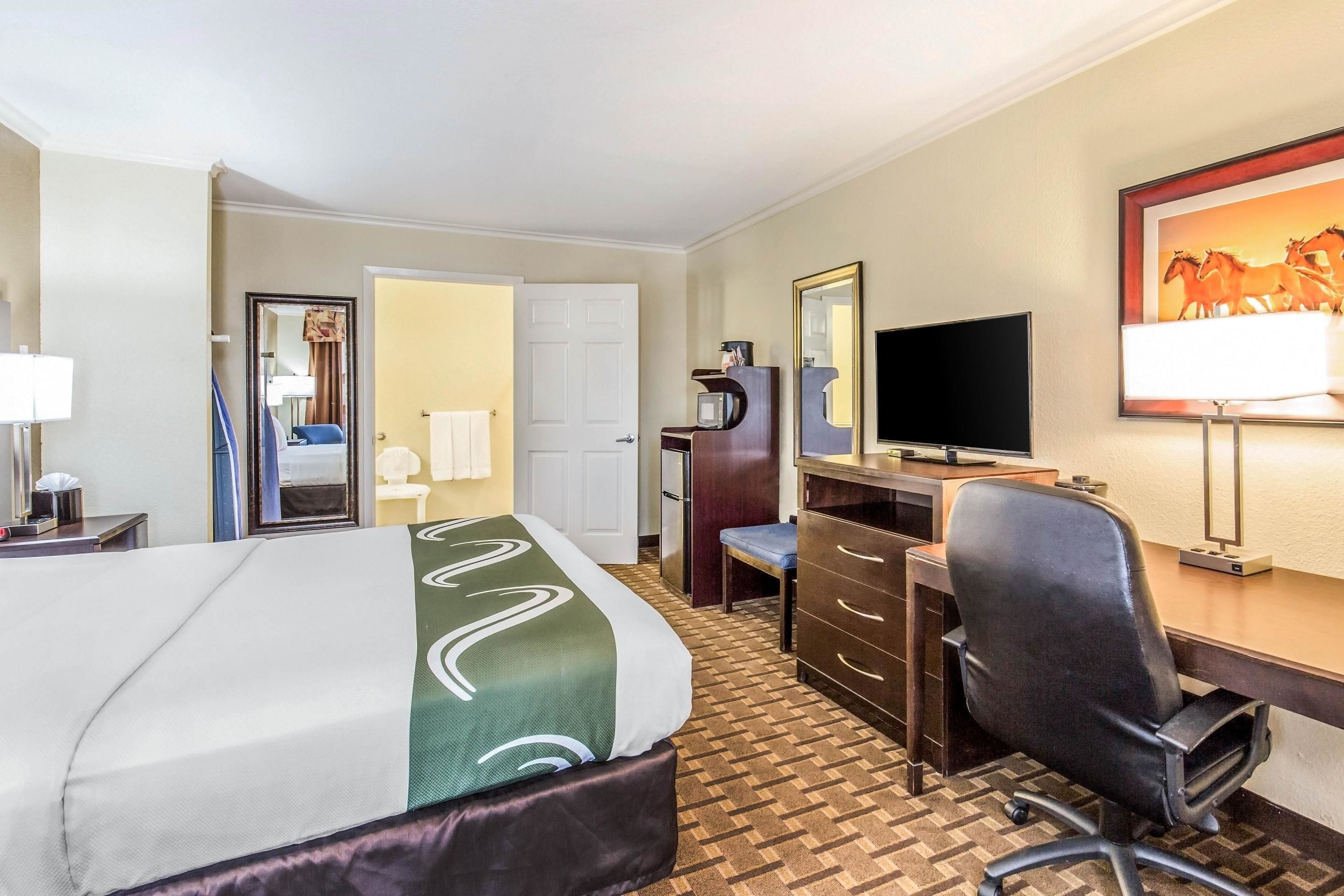 A hotel room with a bed, desk, chair, television, and a mirror.
