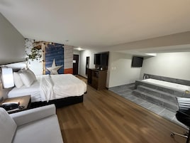Habitación de hotel con cama, escritorio, silla, televisor y baño con bañera, además de una escalera.