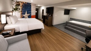 A modern hotel room with a large bed, a desk with a telephone, a flat-screen TV, a built-in TV, a small kitchenette, and a separate bathroom with a bathtub. - Clarion Pointe Addison - Dallas North (Dallas)