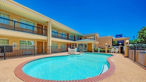 Un hotel con piscina rodeada por una terraza de ladrillo, un patio cubierto y un edificio de dos plantas con balcones.