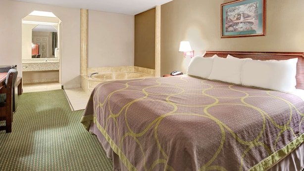 Habitación de hotel con una cama grande, baño con bañera, escritorio y espejo.