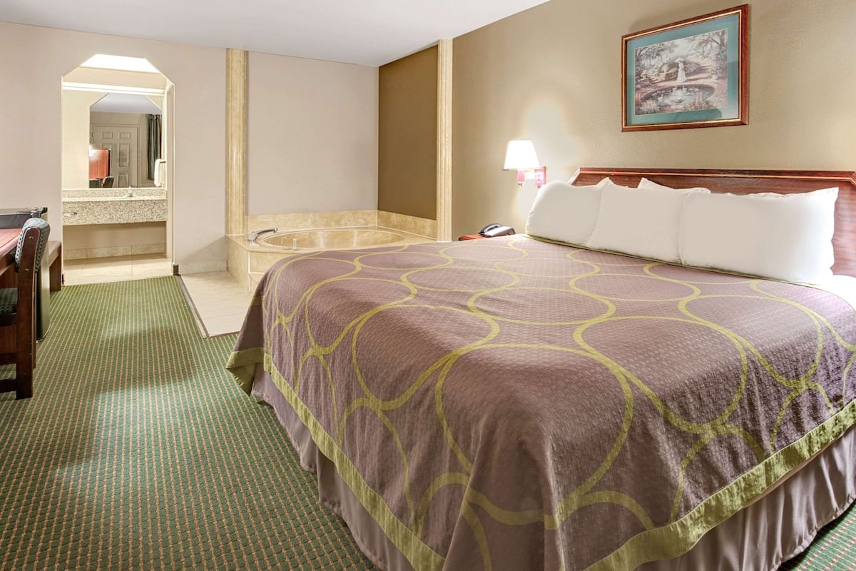 Habitación de hotel con una cama grande, baño con bañera, escritorio y espejo.