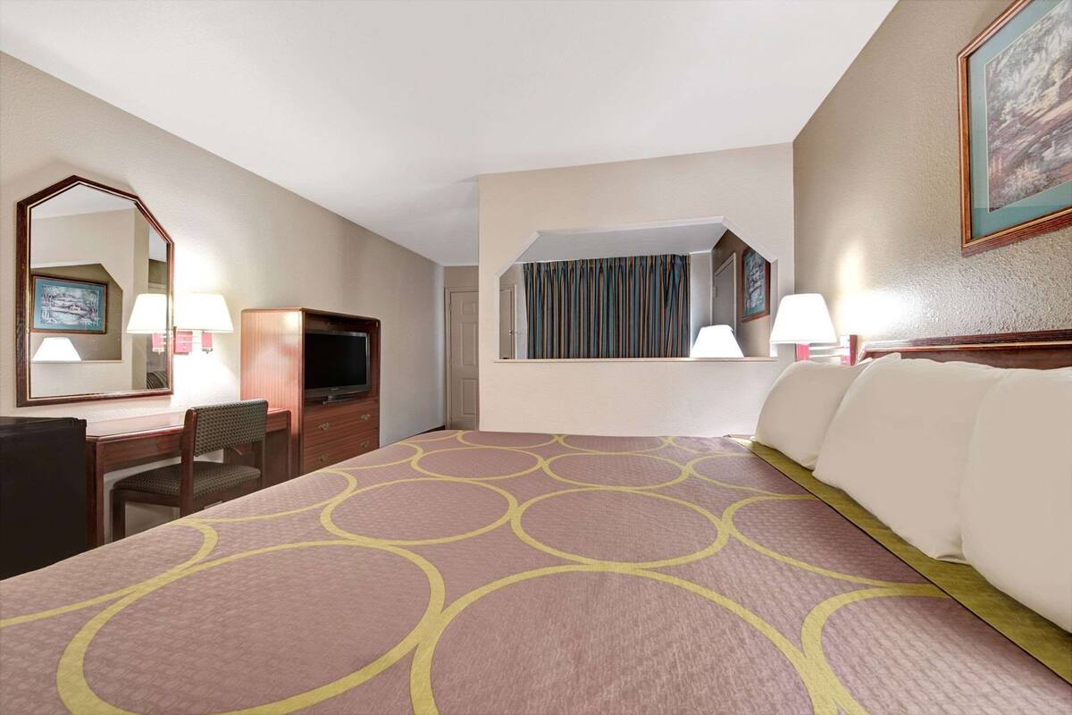 Una habitación de hotel con cama, escritorio, televisor, espejo y ventana con cortinas.