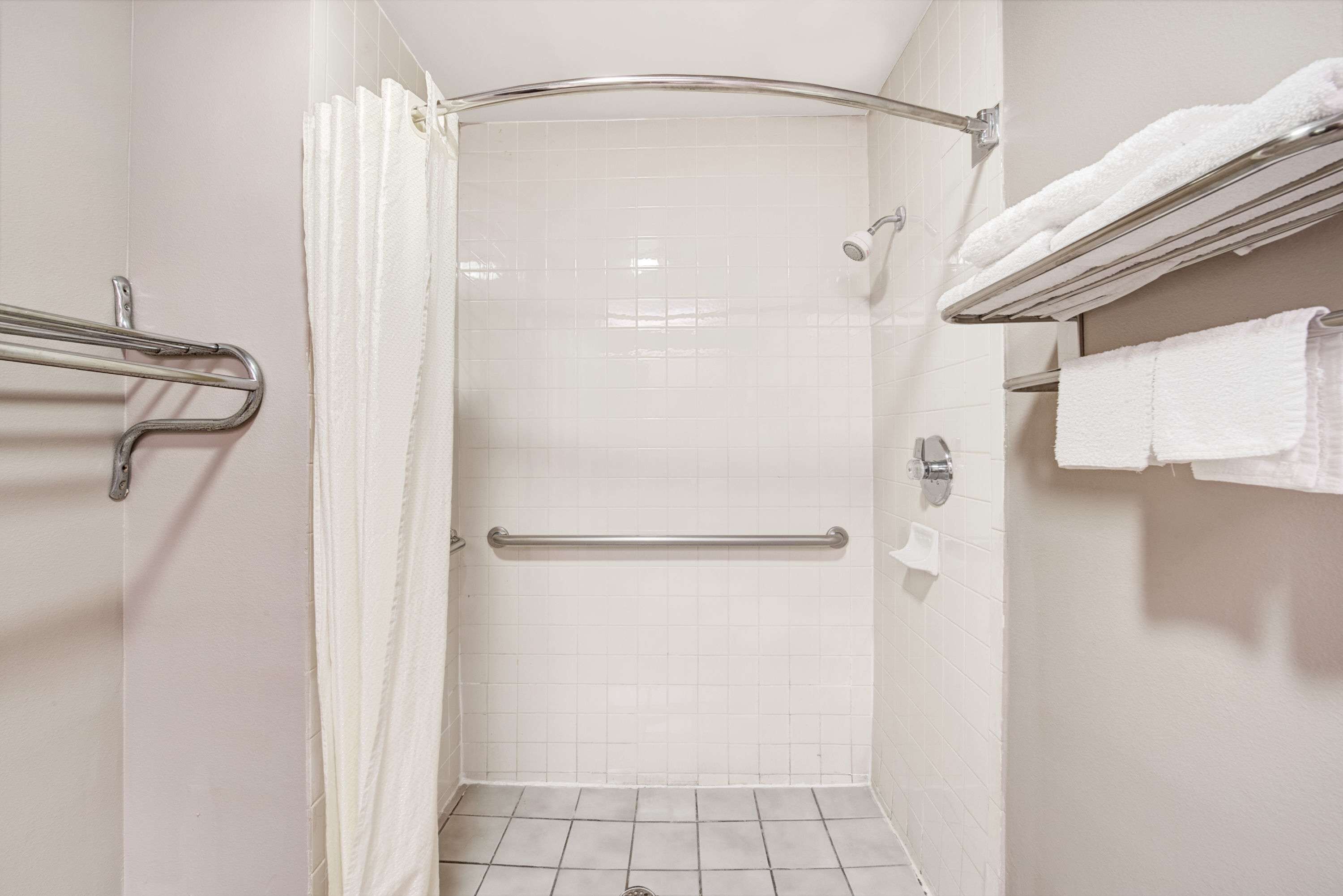 A bathroom with a shower, grab bars, a towel rack, and a toilet paper holder.