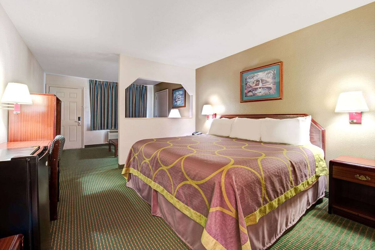 Habitación de hotel con cama, escritorio, silla, espejo, un cuadro y lámpara.