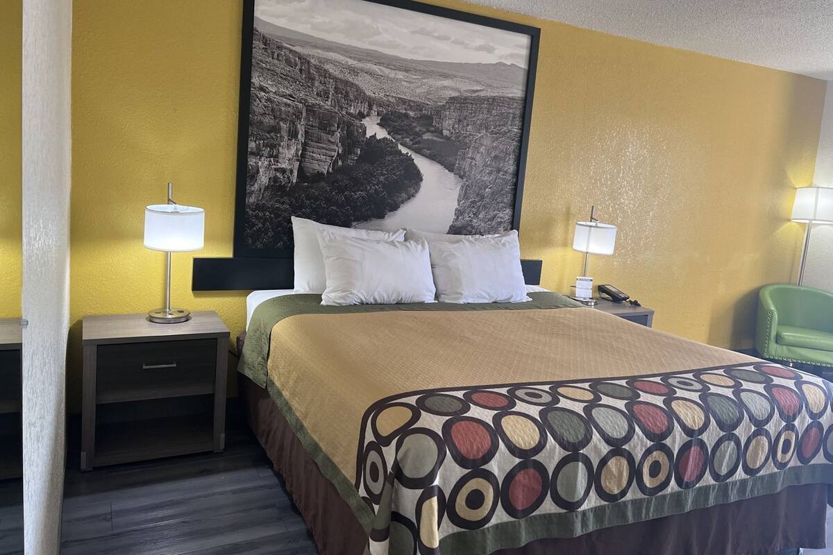 Een hotelkamer met een bed, twee nachtkastjes, een groene stoel en een groot landschap op de muur.