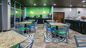 Un restaurant avec plusieurs tables et chaises, un comptoir avec une machine à café et un mur recouvert de carreaux verts.