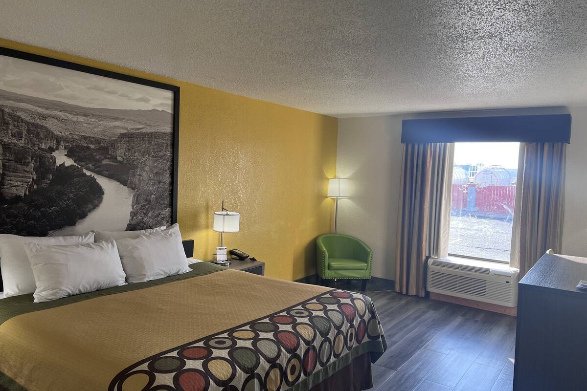 Hotelkamer met een bed, nachtkastje, lamp, groene stoel en een raam met gordijnen.
