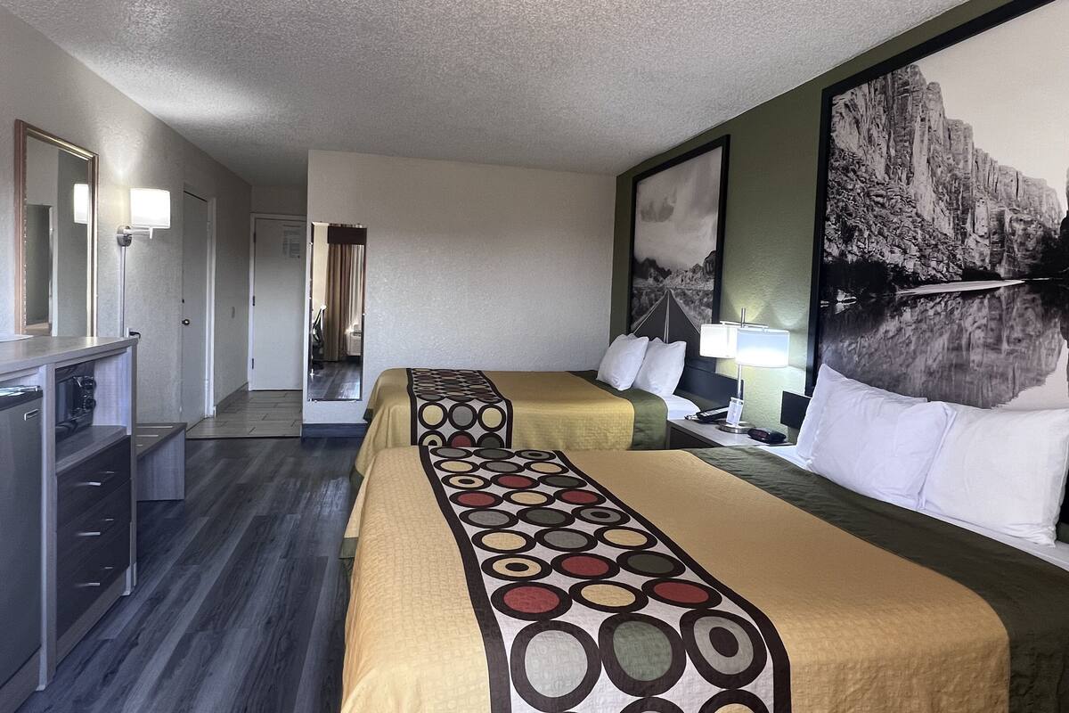 Een hotelkamer met twee bedden, een bureau en een spiegel. Op de muur hangt een schilderij en er is een raam met gordijnen.