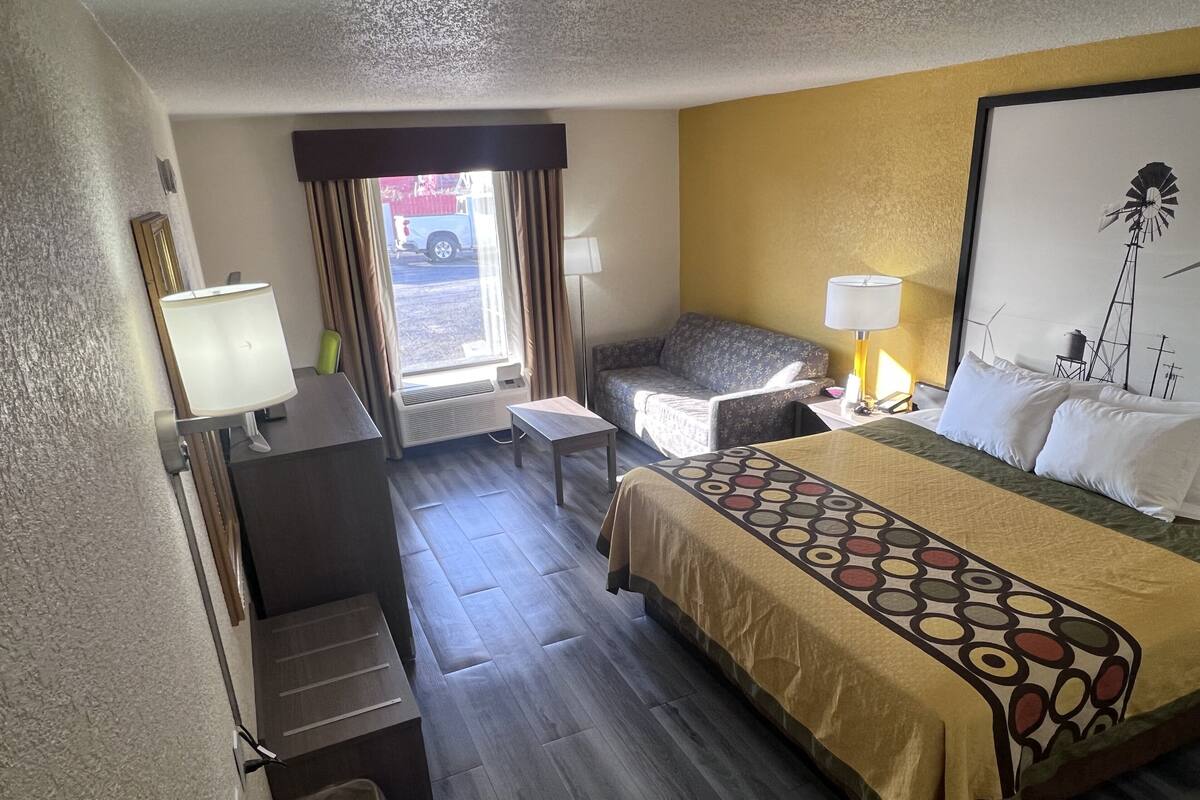 Een hotelkamer met een bed, een bureau, een stoel, een lamp en een raam met gordijnen.