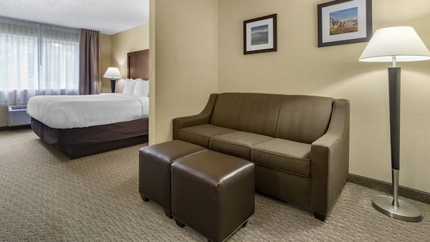 Une chambre d’hôtel comprenant un lit, un canapé, un pouf et deux lampes.