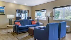 Un salon moderne avec un canapé bleu, un fauteuil assorti, une petite table et une grande fenêtre offrant une vue sur l’extérieur.
