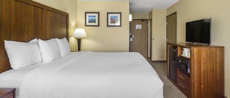 Quarto de hotel com uma cama grande, uma televisão, uma secretária com uma lâmpada e um micro-ondas.