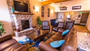 A cozy lobby with a stone fireplace, leather sofas, patterned chairs, and a television mounted above the fireplace.