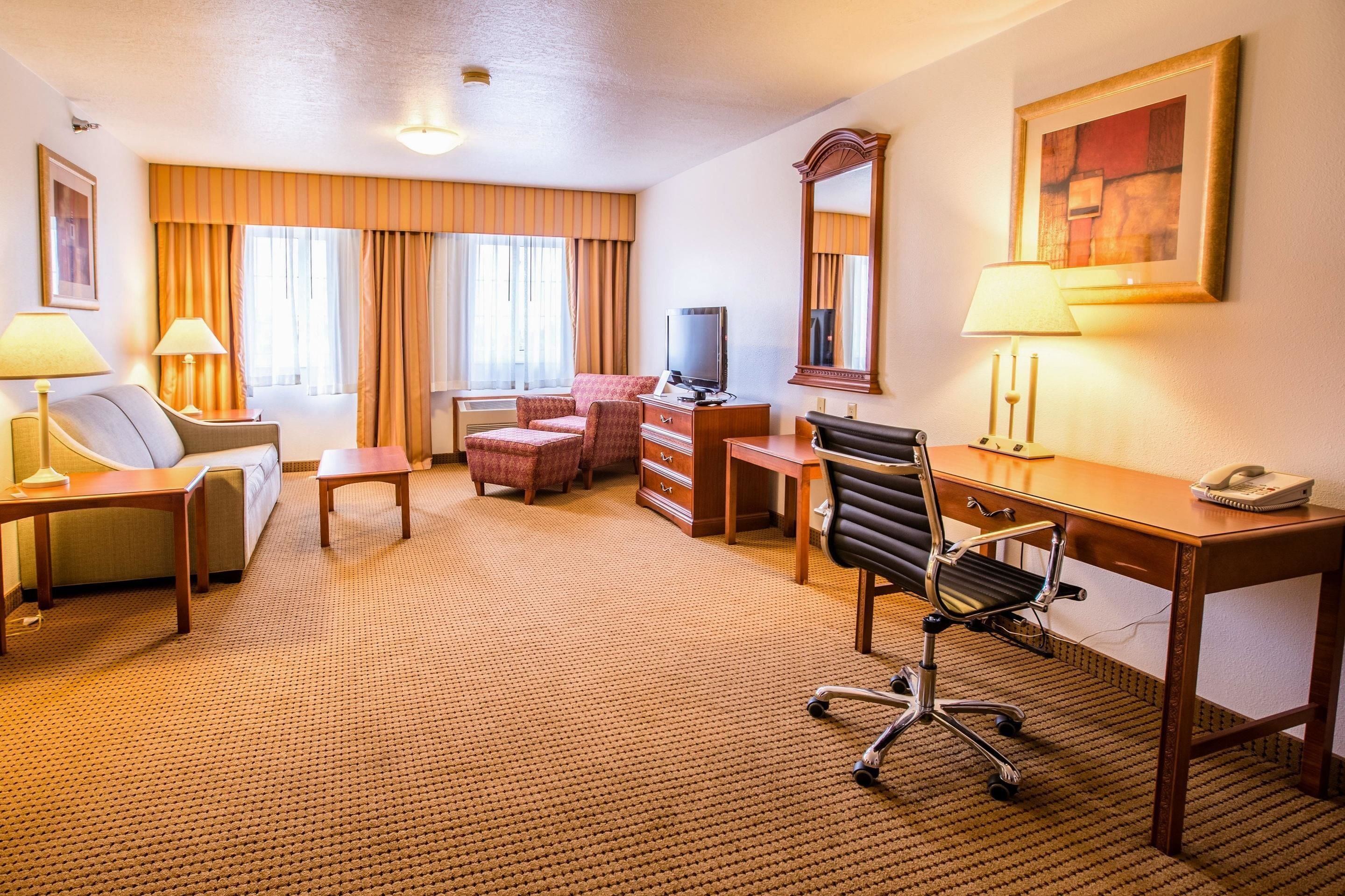 A hotel room with a sofa, a desk, a chair, a television, and a lamp.
