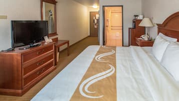Una habitación de hotel con una cama grande, un televisor sobre una cómoda de madera, un espejo y un baño visible a través de una puerta abierta.