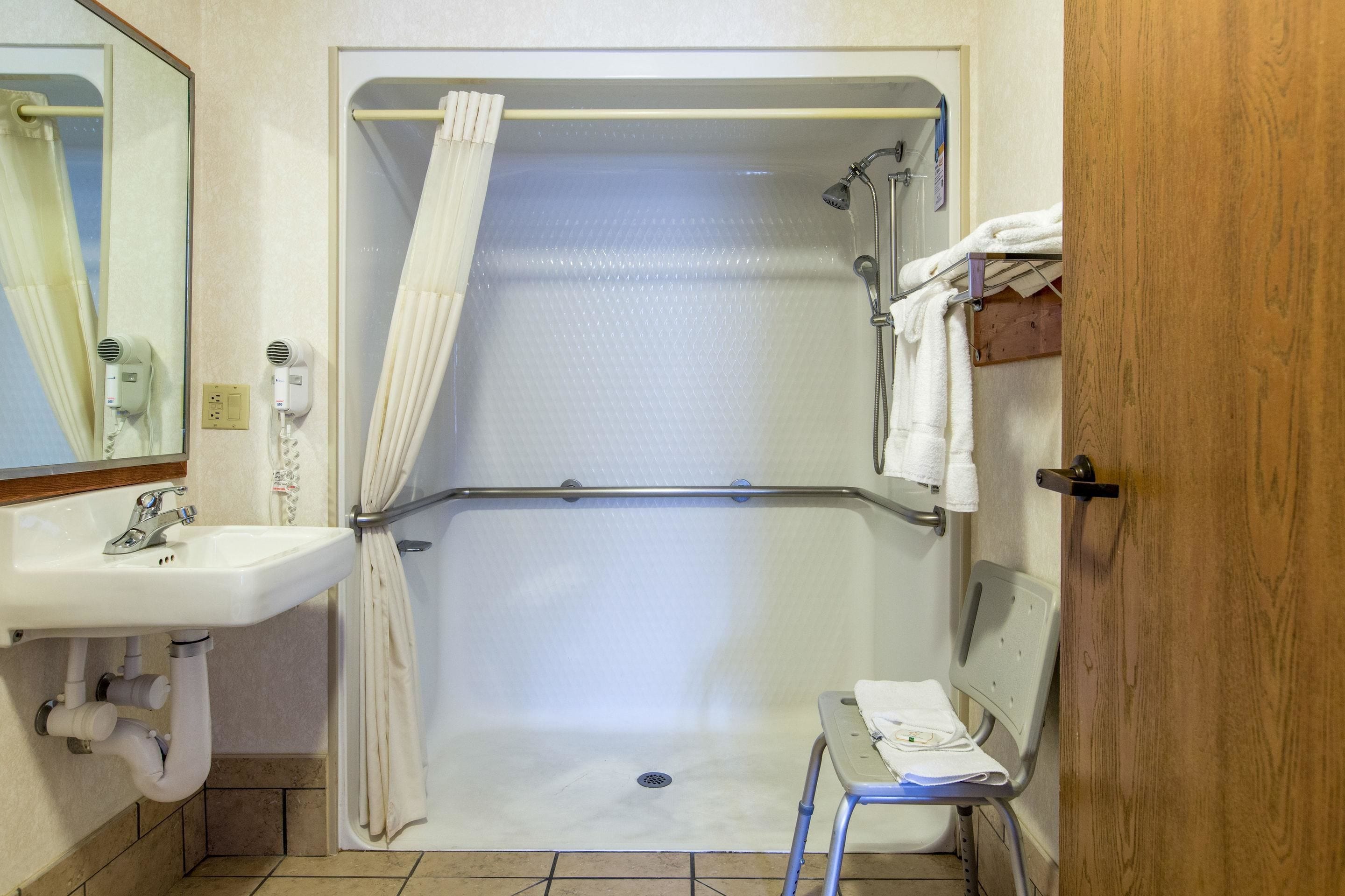 Un baño con ducha, lavamanos, espejo y una silla.