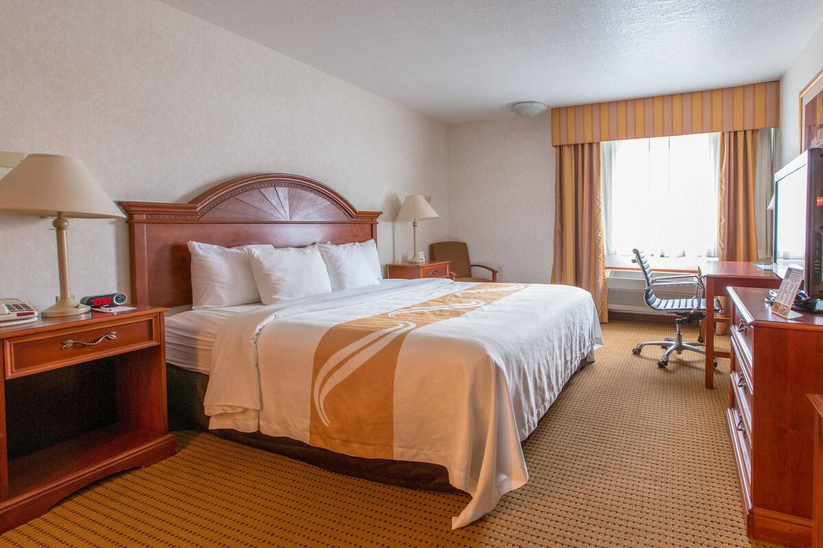 A hotel room with a large bed, two bedside tables with lamps, a desk with a chair, and a television.