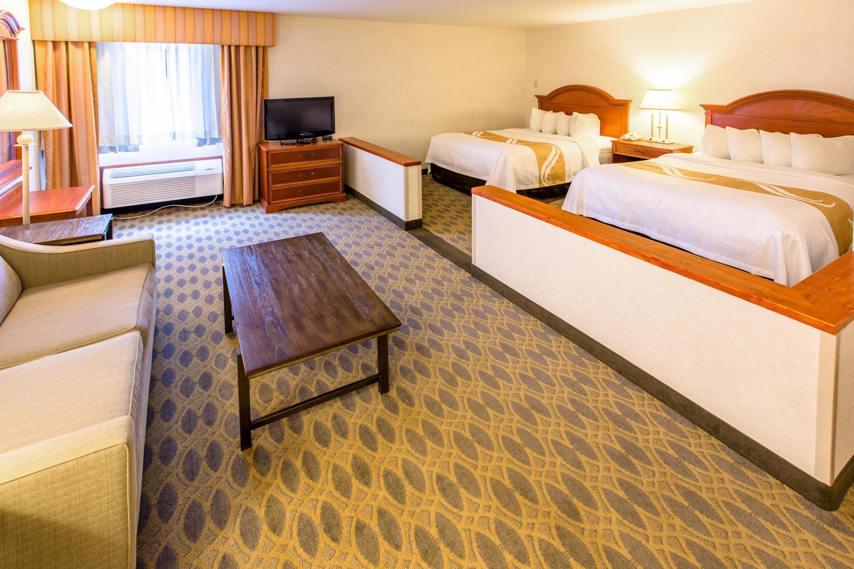A hotel room with two beds, a TV, a desk, and a sofa.