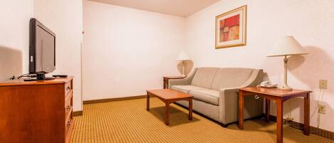 A hotel room with a sofa, a wooden table, a TV on a wooden cabinet, and two lamps.
