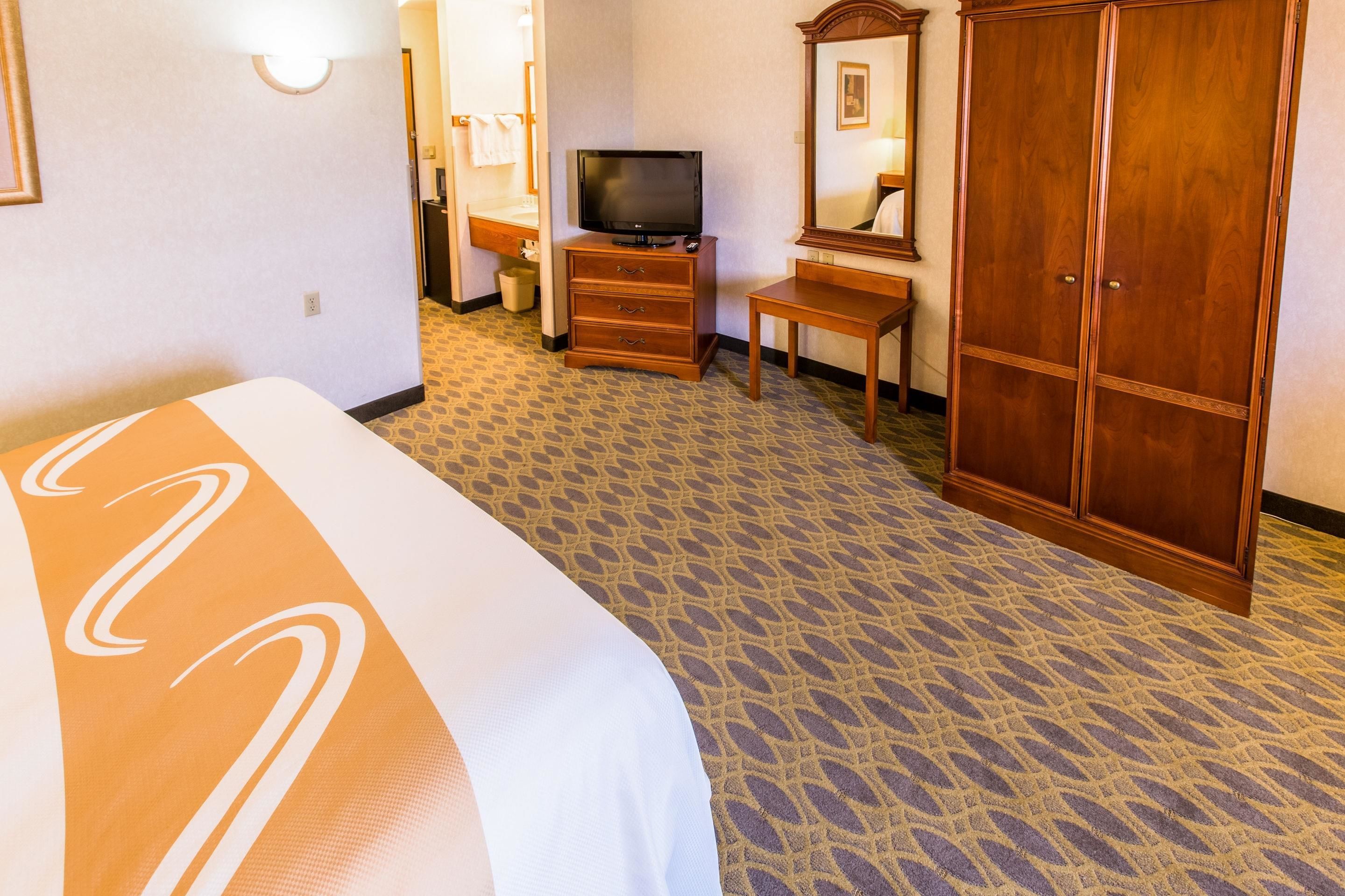 A hotel room with a bed, a television on a wooden dresser, a mirror, and a wardrobe.