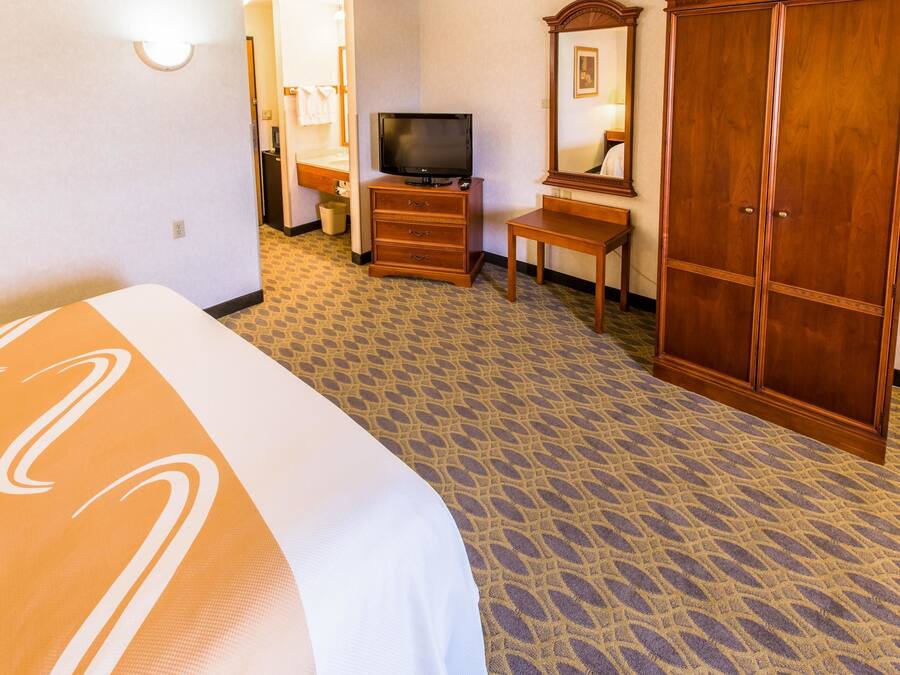 A hotel room with a bed, a television on a wooden dresser, a mirror, and a wardrobe.