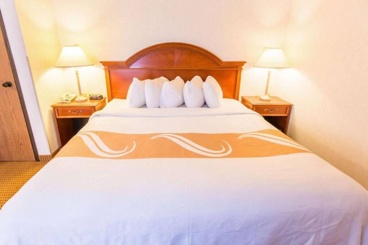A hotel room with a bed, two bedside tables, a wooden headboard, and two lamps.