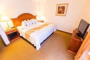 A hotel room with a bed, bedside lamps, a television, and a framed picture on the wall. - Quality Inn & Suites University (Laramie)