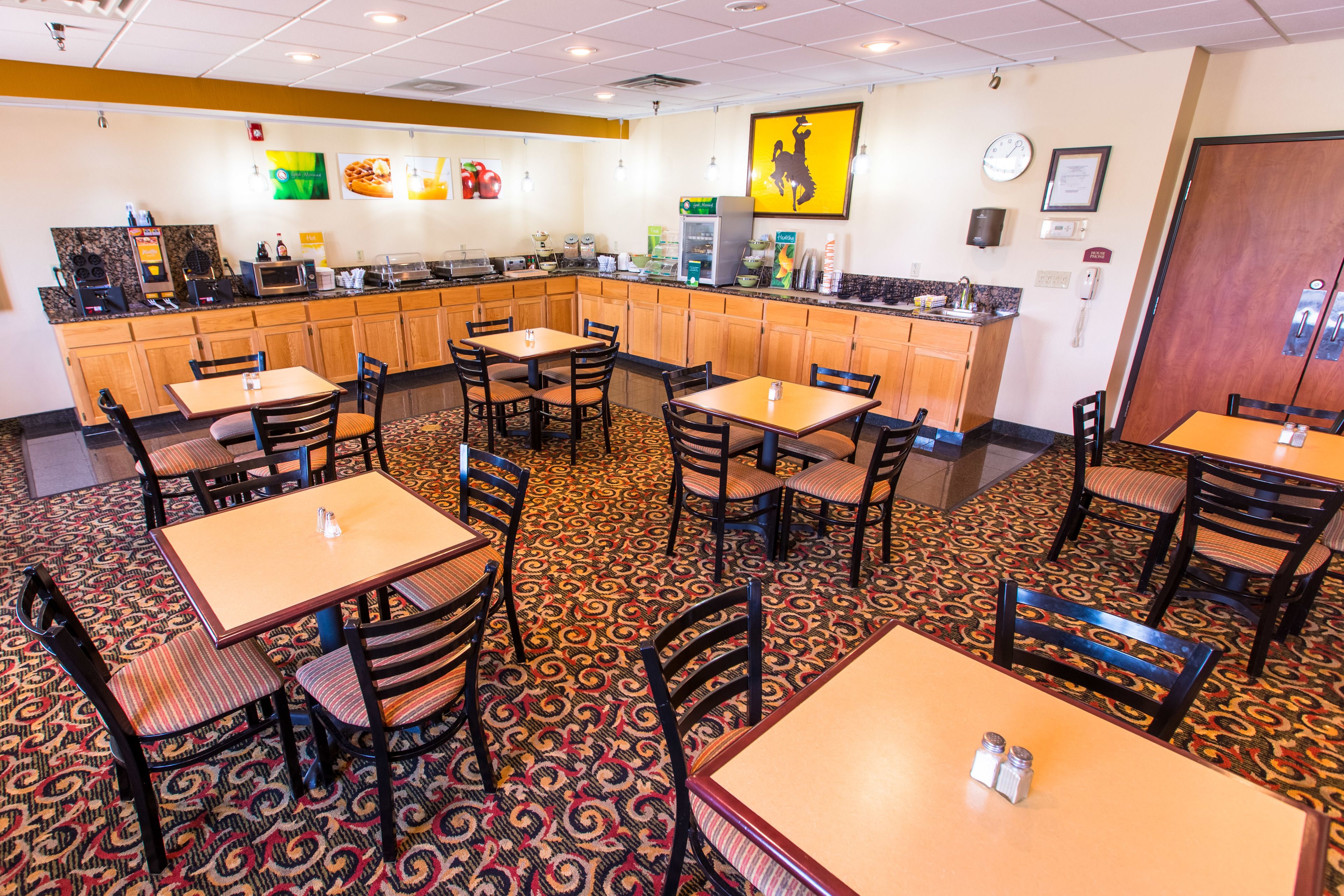 A restaurant with multiple tables and chairs, a kitchen area, and a patterned carpet.