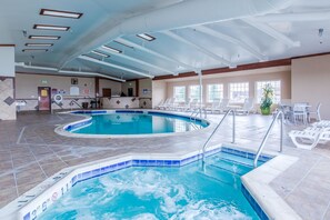 An indoor swimming pool with clear water, tiled flooring, and a sunlit area with chairs and a plant. - Quality Inn & Suites University (Laramie)
