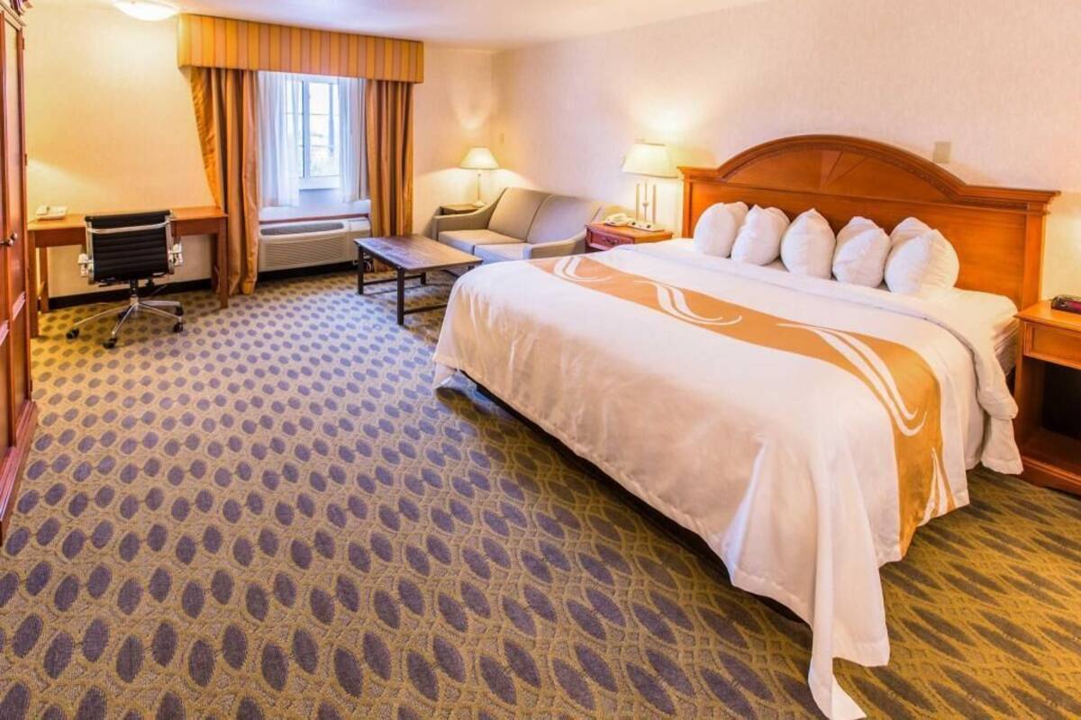 A hotel room with a large bed, a desk, a chair, and a window with curtains.