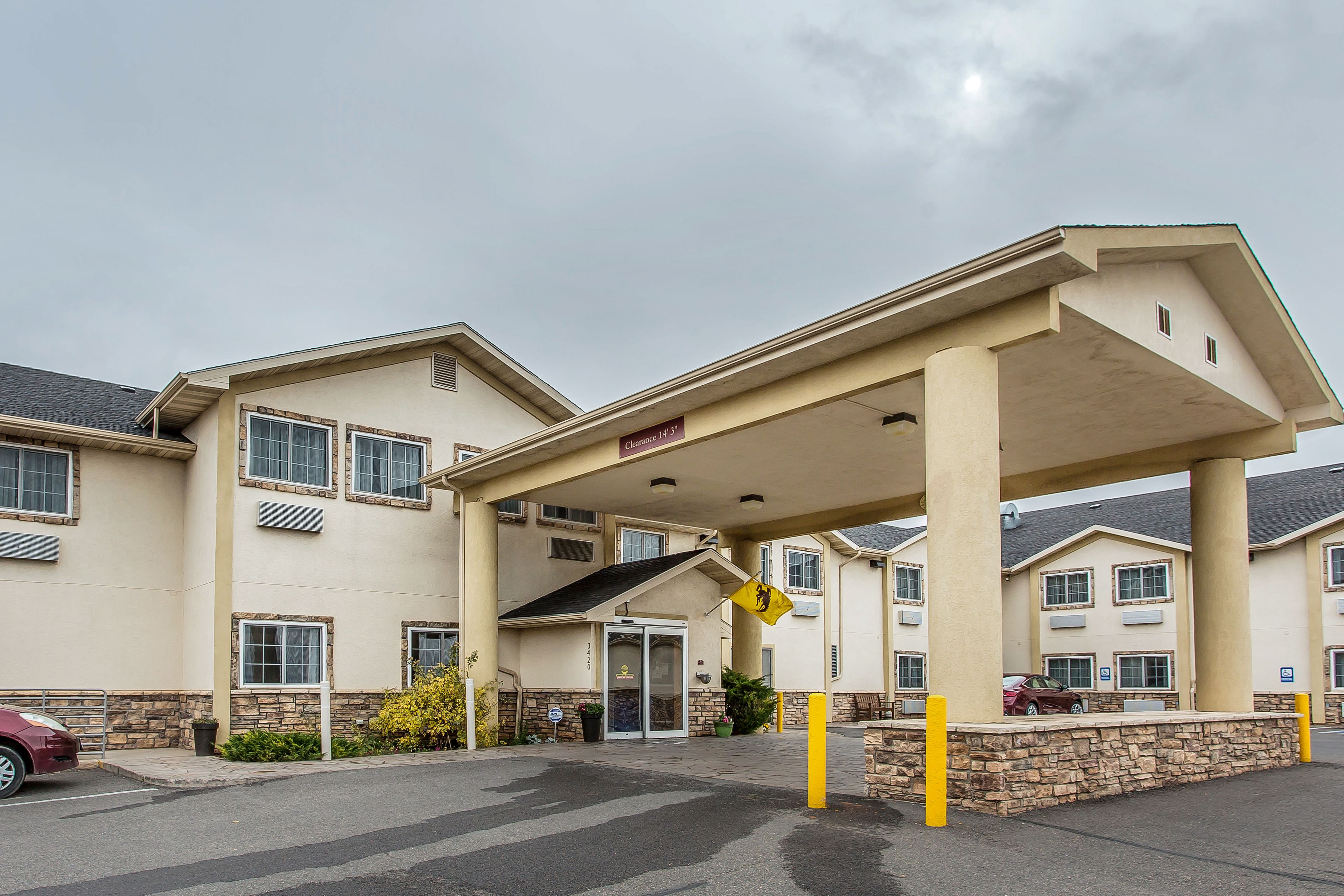 Entrada de hotel con un vestíbulo cubierto, zona de estacionamiento y fachada con numerosas ventanas y un letrero que indica disponibilidad de habitaciones.