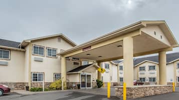 Entrada de hotel con un vestíbulo cubierto, zona de estacionamiento y fachada con numerosas ventanas y un letrero que indica disponibilidad de habitaciones.
