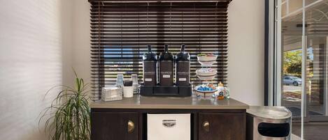 A kitchenette with a coffee maker, a bowl of fruit, and a trash can.
