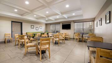 A dining area with wooden chairs and tables, recessed ceiling lights, and a television mounted on the wall.