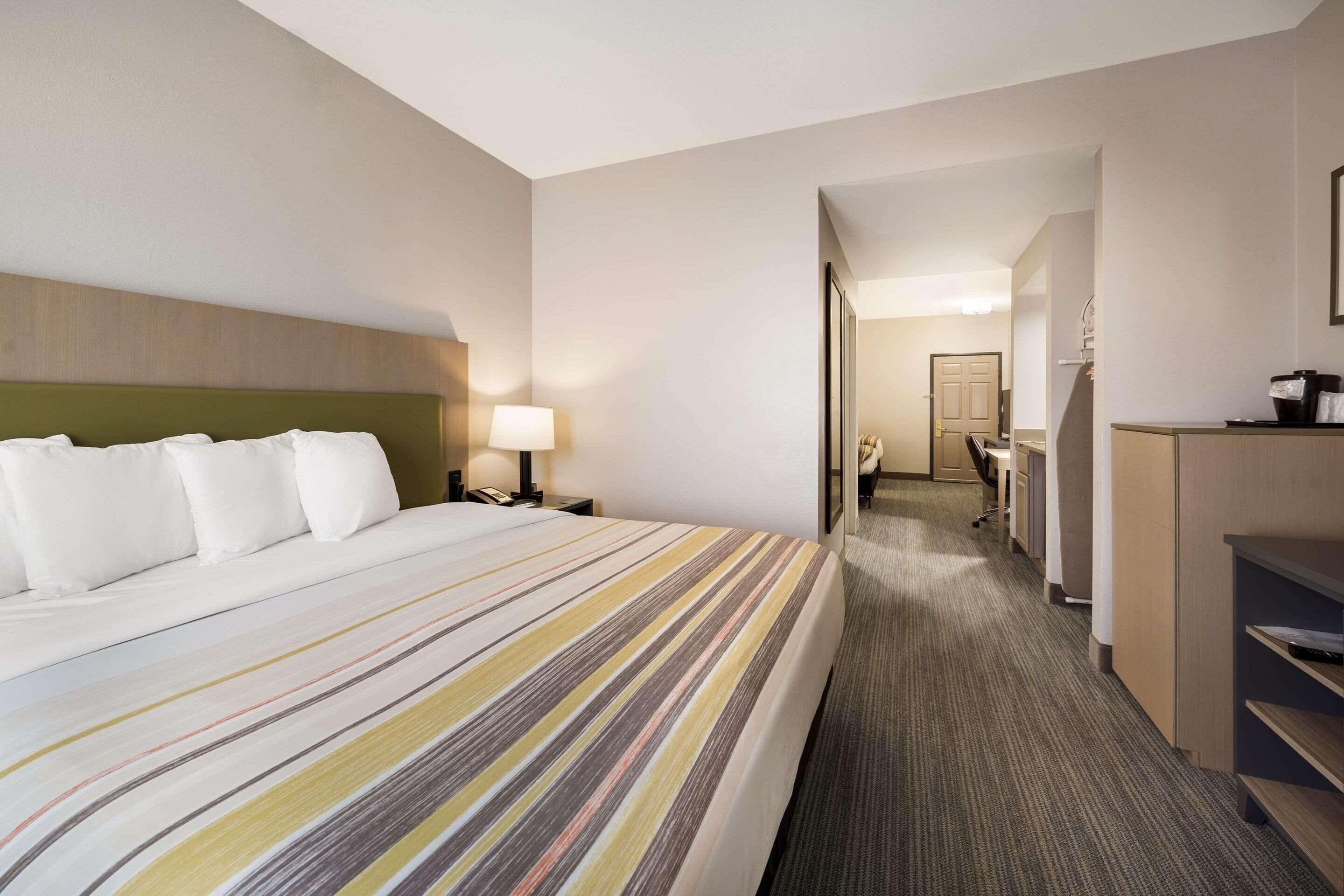 Habitación de hotel con una cama grande, un escritorio, una silla y un baño visible a través de una puerta abierta.