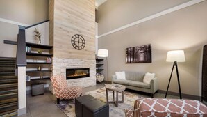 A modern living room with a fireplace, a sofa, a patterned armchair, and a coffee table. - Country Inn & Suites by Radisson, Freeport, IL (Freeport)