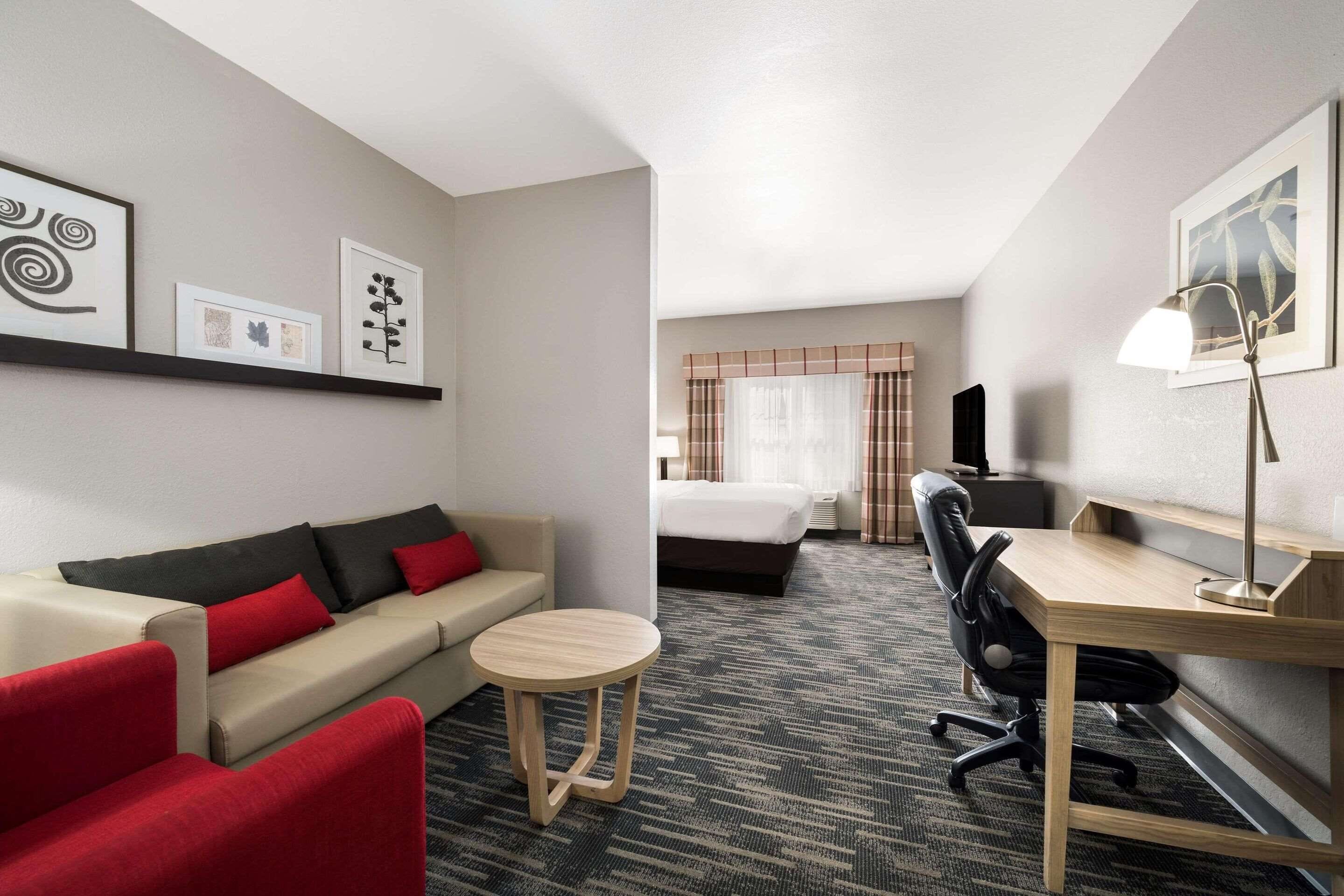 A hotel room with a sofa, a small round table, a desk with a chair, a bed, and a TV.