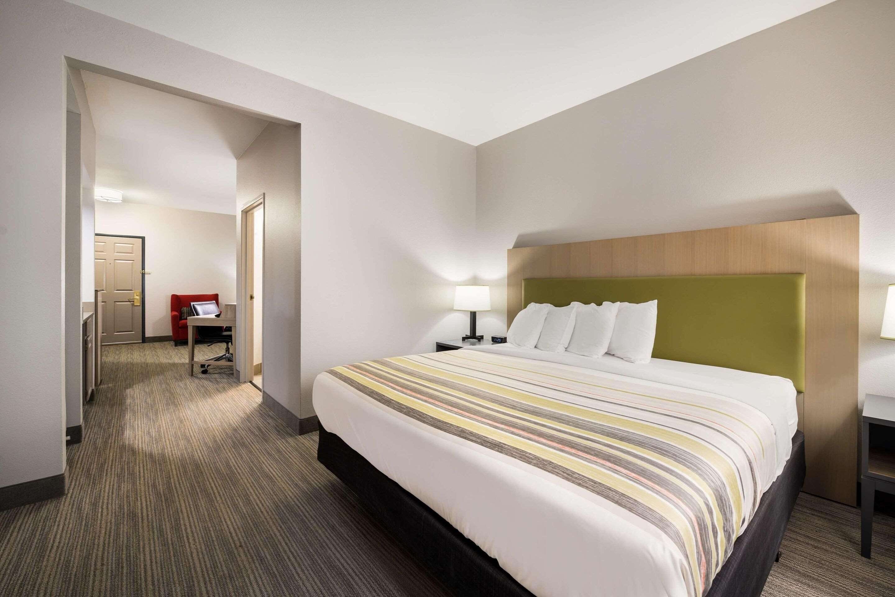 Habitación de hotel con una cama grande, un escritorio, una silla y una puerta que da a un pasillo.