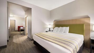 Habitación de hotel con una cama grande, un escritorio, una silla y una puerta que da a un pasillo.