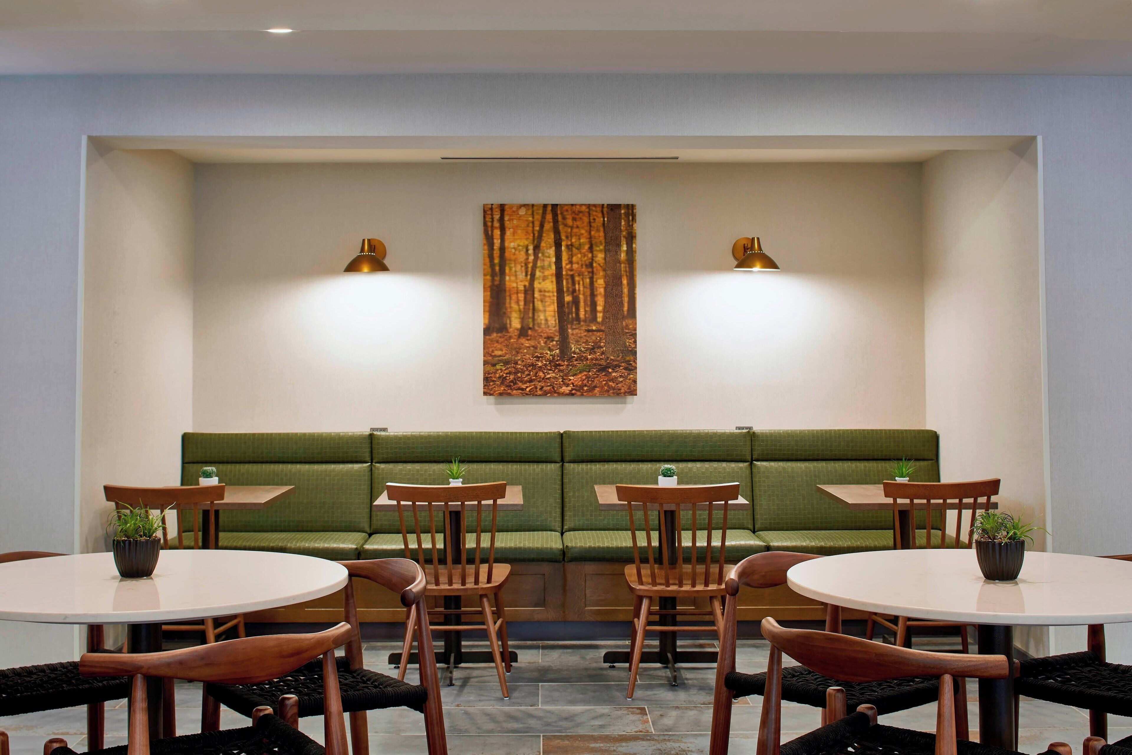 A dining area with green cushioned seating, wooden tables, and chairs, and two wall-mounted lamps.