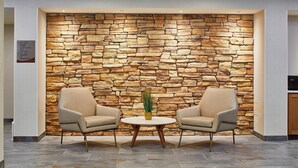 Eine Lobby mit Steinwand, zwei Sesseln, einem kleinen Tisch und einer Zimmerpflanze.