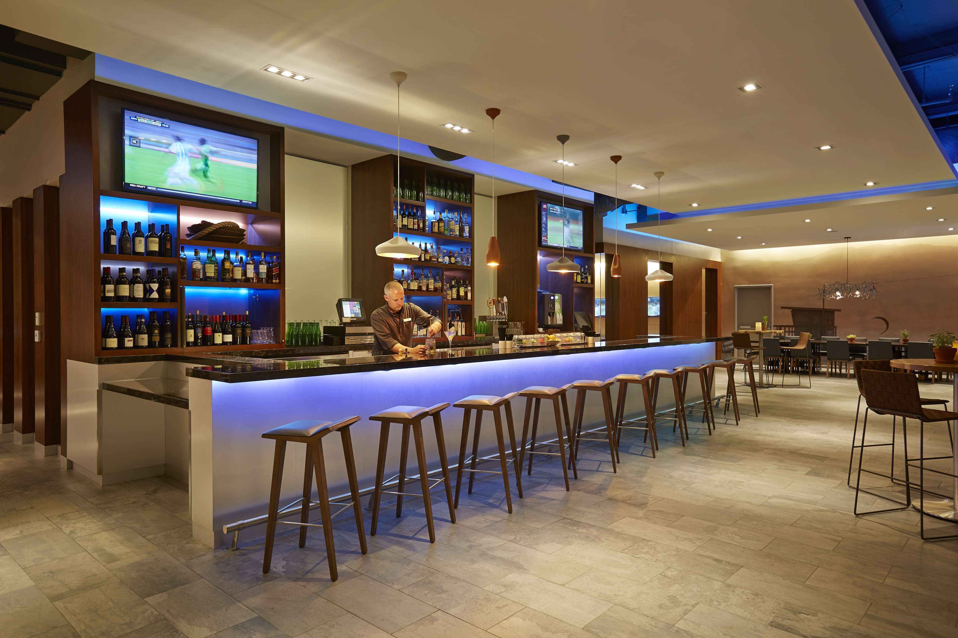 A modern bar area with a long counter, multiple stools, and a bartender.