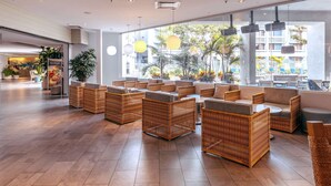 A spacious lobby with wicker furniture, large windows offering a view of the outdoors, and a reception area in the background. - Hotel MDR Marina del Rey - a DoubleTree by Hilton (Marina del Rey)