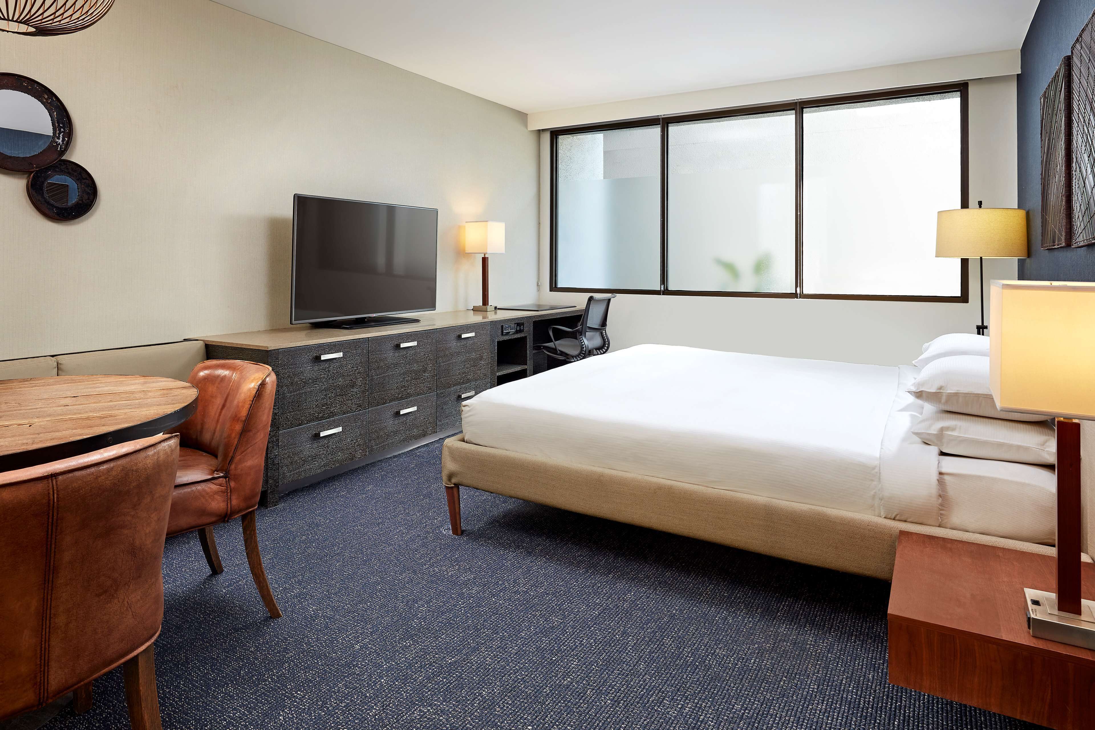 Una habitación de hotel con cama, escritorio con televisor, silla y lámpara.