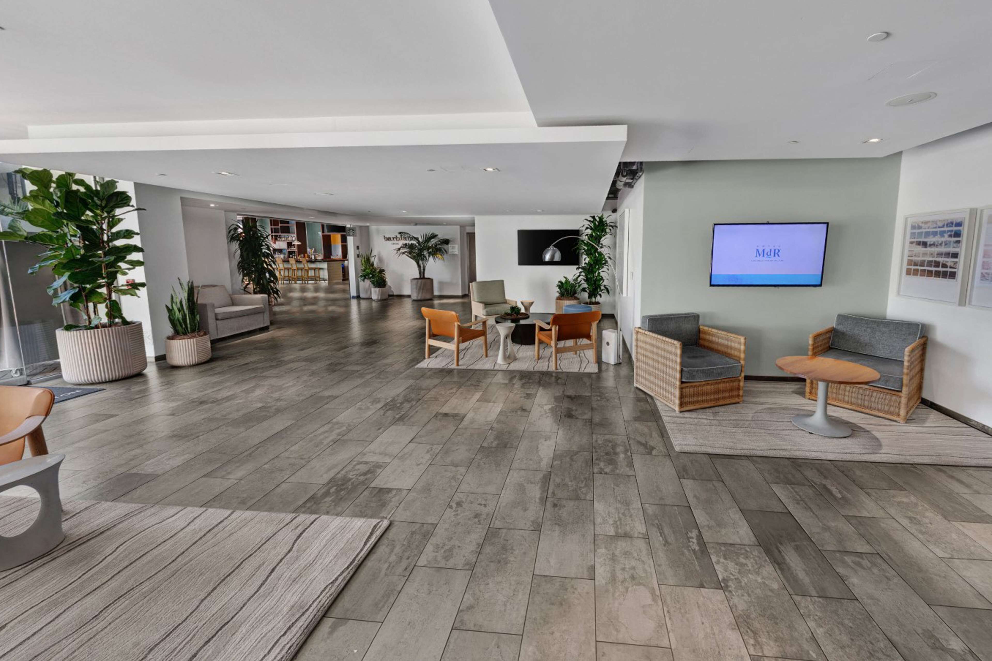 Un vestíbulo amplio con un diseño moderno, que cuenta con un gran espacio de estar con sofás y sillones, un televisor de pantalla plana en la pared y una variedad de plantas en macetas.