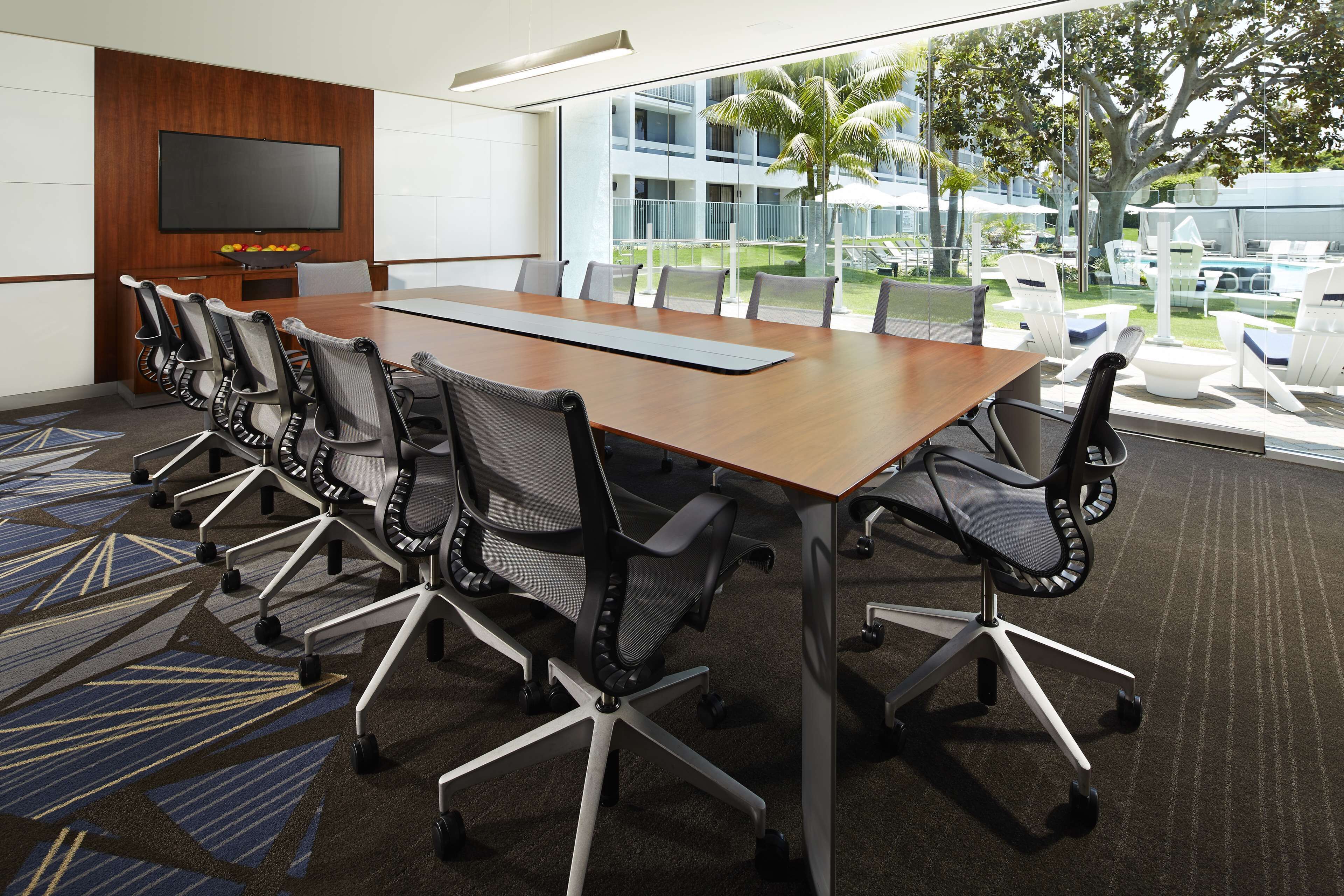 A conference room with a long table, chairs, a TV, and a view of a pool and building.